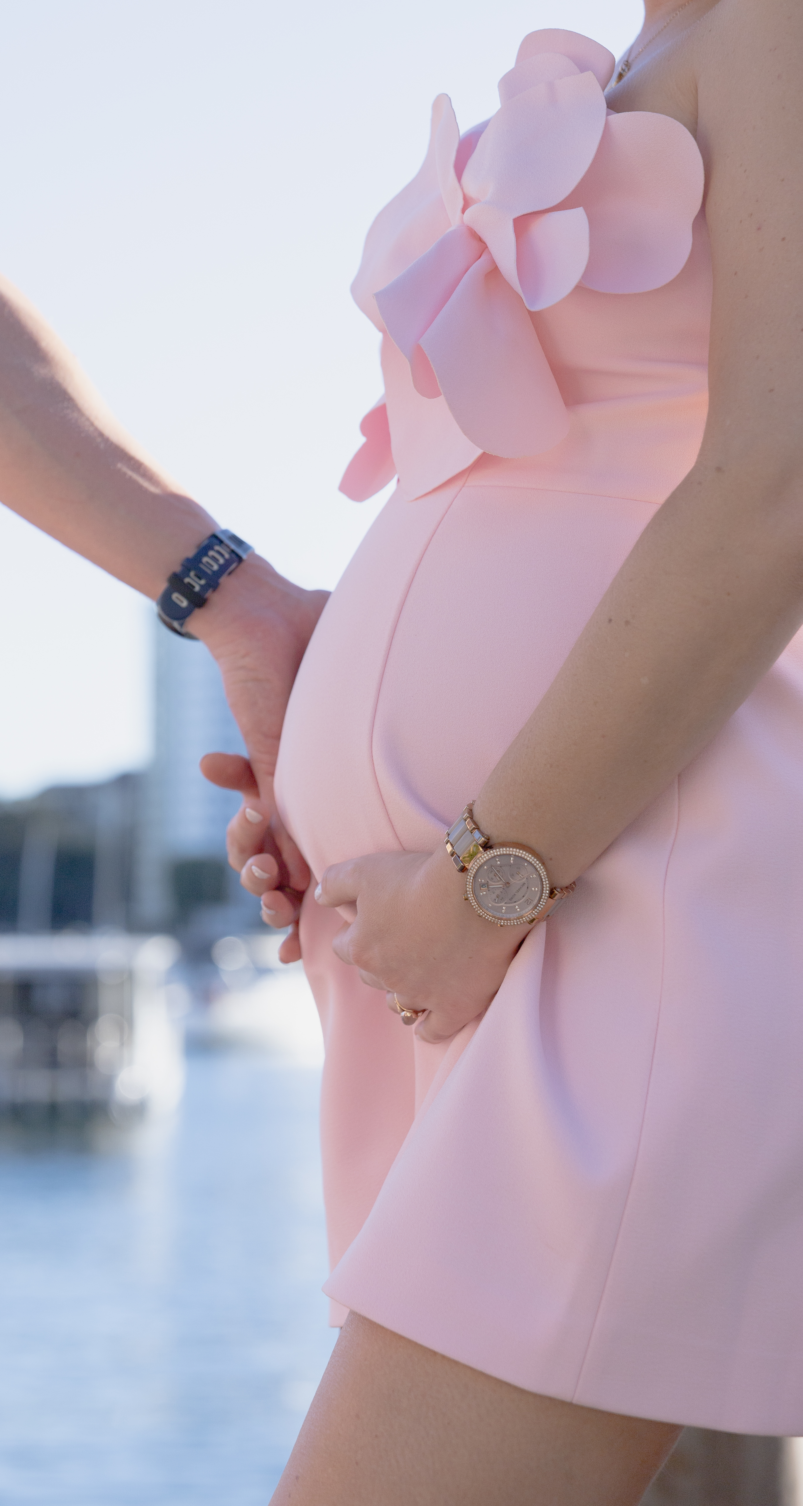 close-up side view of a pregnant woman in a pink dress holding her belly, with a man's hand gently resting over hers